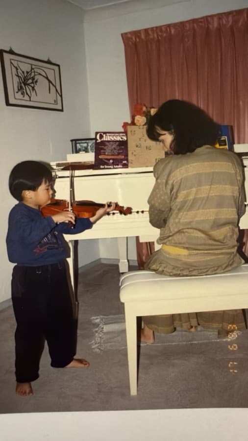 A young Ray Chen playing violin beside his mum at the piano